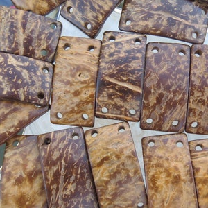 May include: A collection of rectangular coconut shell pieces with a brown and tan marbled pattern. Each piece has four holes drilled through it.