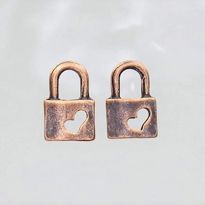May include: Two small copper-colored padlocks with heart-shaped cutouts. The padlocks are about 1 inch in size.