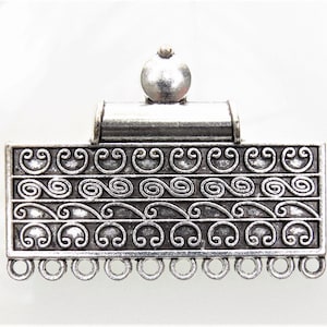 May include: Silver-toned metal clasp with a decorative scroll design and a round top. The clasp has a row of loops at the bottom.