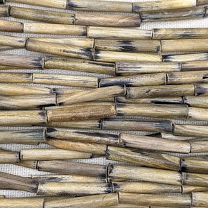 Op de afbeelding: Close-up van een geweven patroon van houten kralen. De kralen zijn cilindrisch met een natuurlijke houtnerf afwerking, variërend in tinten van bruin, bruin en zwart. De kralen zijn gerangschikt in een horizontaal patroon, waardoor een textuur ontstaat.