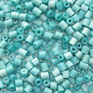 May include: A large quantity of turquoise blue glass beads. The beads are cylindrical in shape with a hole in the center. The beads are all the same size and shape.