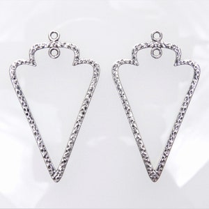 Könnte beinhalten: Zwei silberne dreieckige Ohrringrohlinge mit strukturierter Oberfläche. Jeder Rohling hat oben eine Öse zum Anbringen von Ohrringdrähten.