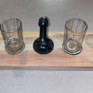 May include: A wooden serving tray with four glass cups and a black metal pipe fitting in the center. The tray is made of light wood with a natural finish.