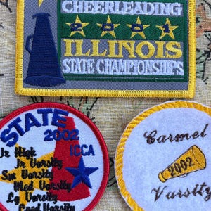 May include: Three embroidered patches with text and designs. The largest patch reads "ICCA Cheerleading Illinois State Championships." Two smaller patches say "State 2002" and "Carmel Varsity 2002."