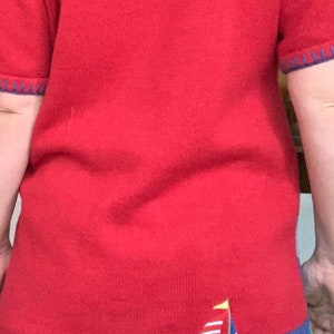 Puede incluir: Su&eacute;ter de punto rojo con un dise&ntilde;o de velero azul y blanco en el dobladillo inferior.