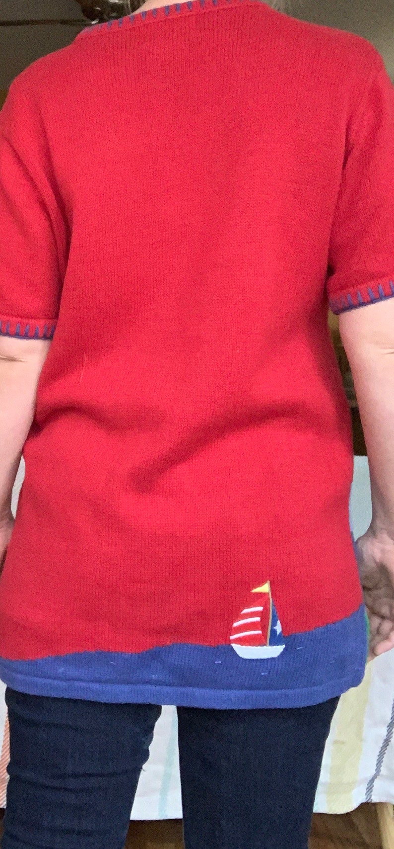 Puede incluir: Su&eacute;ter de punto rojo con un dise&ntilde;o de velero azul y blanco en el dobladillo inferior.