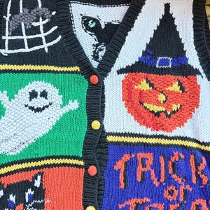 May include: A black knit vest featuring a Halloween theme with colorful intarsia designs including a white ghost on green, a black cat on red, a jack-o'-lantern on light blue, and the text "TRICK or TREAT" in orange on a blue background.