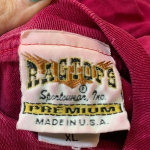 May include: A red t-shirt with a white tag that reads "Ragtop&reg; Sportwear, Inc. Premium Made in U.S.A." and a white size tag that reads "XL".