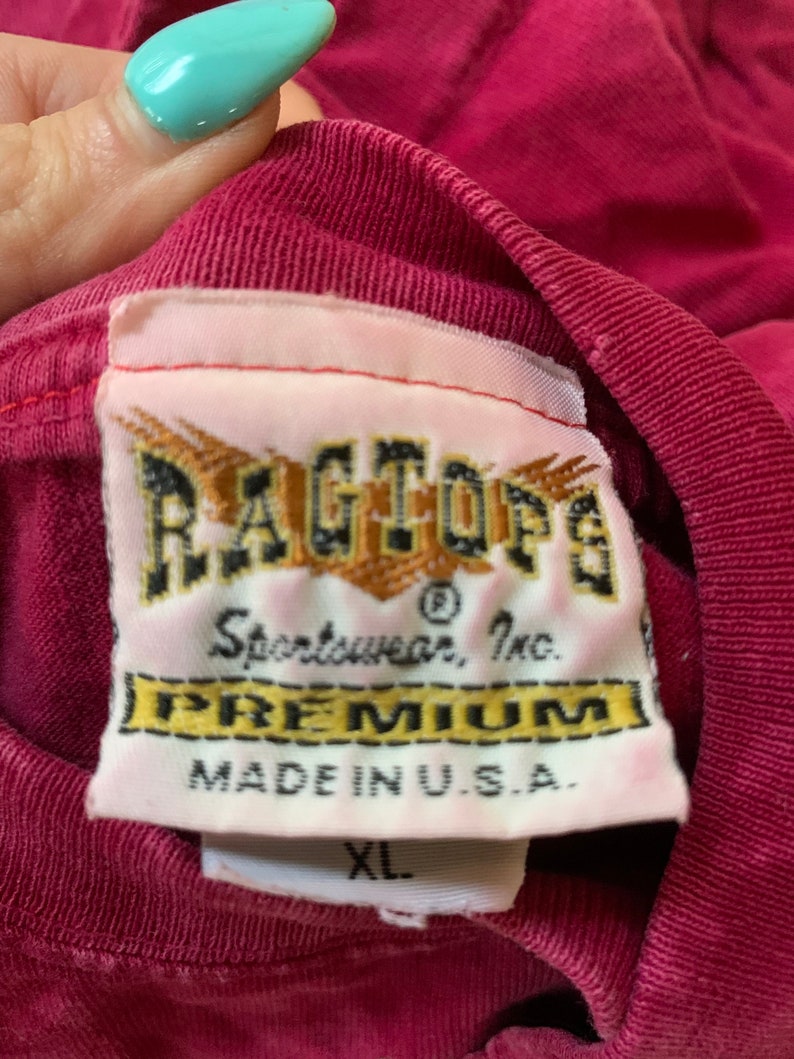May include: A red t-shirt with a white tag that reads "Ragtop&reg; Sportwear, Inc. Premium Made in U.S.A." and a white size tag that reads "XL".
