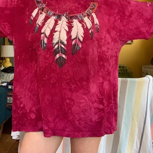 May include: A red tie-dye t-shirt with a colorful Native American inspired feather design on the front.