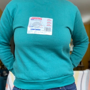 May include: A teal green sweatshirt with a white tag that reads "JERZEES" and "Increased Dimensions".