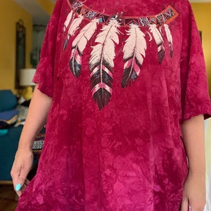 May include: A red tie-dye t-shirt with a Native American inspired design featuring feathers and geometric patterns.
