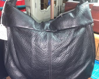 May include: Black leather hobo bag with a textured surface. The bag features a rounded shape, a top handle, and silver-tone metal rings. The bag is displayed on a wooden surface.