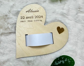 May include: A heart-shaped wooden plaque featuring the engraved name Alessio, the date 22 avril 2024, the time 16h21, the length 50 cm, and the weight 3.070 kg. A small dark wooden heart accent is attached, and a white paper band is inserted.