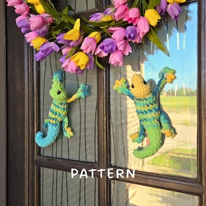 Op de afbeelding: Twee gehaakte hagedisfiguren in tinten groen, blauw en geel zijn bevestigd aan een glazen deur. Daarboven hangt een krans van roze, paarse en gele tulpen. Het woord PATTERN staat in witte letters onderaan de afbeelding.