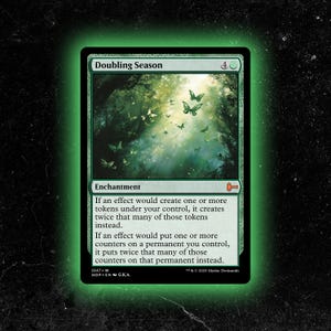 May include: A green Doubling Season card featuring a forest scene with butterflies. The card text describes the enchantment's effect on tokens and counters. The card has a green border and is from Mythic Decksmith.