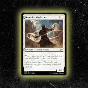 May include: A Drannith Magistrate trading card featuring a human wizard character surrounded by glowing light rings. The card text reads: Your opponents can't cast spells from anywhere other than their hands. It has a power and toughness of 1/3.