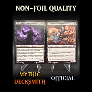 May include: Two Magic: The Gathering trading cards on display. The cards are "Em'kalann, Void Resonator" and "Yahenni, Undying Partisan." The cards are displayed on clear stands against a dark background. The text "NON-FOIL QUALITY," "MYTHIC DECKSMITH," and "OFFICIAL" are visible.