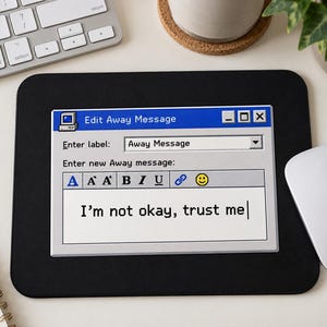 Könnte beinhalten: Ein schwarzes, rechteckiges Mauspad mit einer Retro-Computerfenster-Grafik mit dem Titel Edit Away Message. Die Benutzeroberfläche enthält Textfelder, Formatierungssymbole und den getippten Text I'm not okay, trust me in klassischer Pixelschrift.
