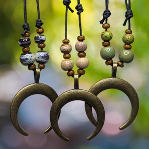 May include: Three necklaces with crescent moon pendants and colorful ceramic beads. The beads are brown, green, and white with black accents.