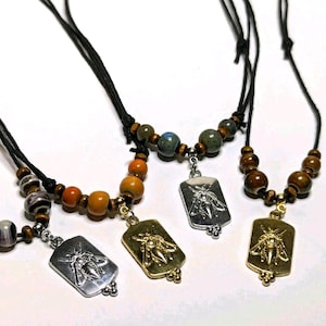 May include: Three necklaces with wooden beads and a pendant featuring a bee design. The pendants are silver, gold, and silver. The necklaces are on a white background.