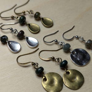 May include: Three pairs of earrings with silver and gold teardrop and round shaped pendants. Each pair features a different colored stone bead.