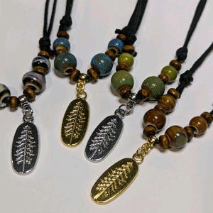 May include: Three necklaces with a tree pendant. Each necklace has a different color scheme of brown, green, and blue ceramic beads. The tree pendants are silver and gold.
