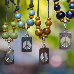 May include: Four necklaces with peace sign charms. Each necklace has different colored ceramic beads, including green, blue, and brown.