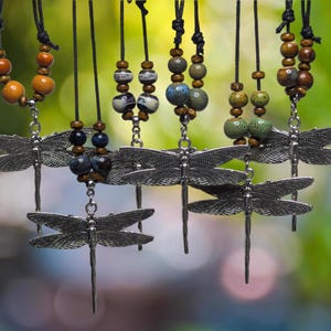 May include: Five necklaces with dragonfly pendants and colourful ceramic beads. The necklaces are made with brown leather cord and feature different colour combinations of beads.