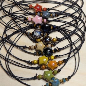 May include: A stack of ten black cord necklaces with star-shaped ceramic beads in various colors, including red, pink, blue, green, yellow, and brown.