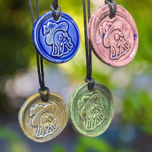 May include: Four ceramic pendants with black cords, each featuring a ghost wearing a witch's hat. The pendants are in shades of blue, purple, green, and yellow.