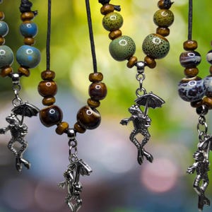 May include: Four necklaces with frog charms hanging from them. Each necklace has brown wooden beads and colorful glass beads. The frogs are holding umbrellas.