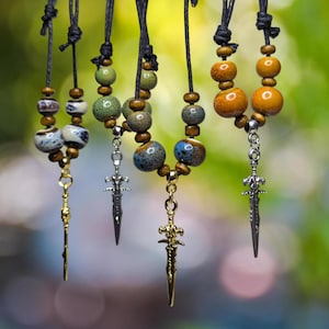 Può includere: Cinque collane con ciondoli a forma di spada e perline in ceramica colorate. Le perline sono in tonalità di verde, arancione, blu e marrone.
