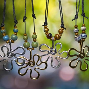 Może przedstawiać: Pięć naszyjników z srebrnymi i złotymi zawieszkami w kształcie kwiatów. Każdy naszyjnik zdobią kolorowe ceramiczne koraliki w odcieniach niebieskiego, zielonego i brązowego.