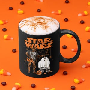 Peut inclure: Mug à café noir avec un dessus mousseux blanc et un motif Star Wars sur le thème d'Halloween. Le motif représente un squelette habillé en Stormtrooper et un fantôme habillé en Dark Vador tenant une citrouille. Le texte "STAR WARS" est imprimé sur la tasse.