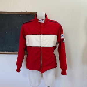 Puede incluir: Chaqueta de carreras roja con una franja blanca en el pecho y cuello negro. La chaqueta tiene el texto "Auto Pro" en el cuello y un parche en la manga. La chaqueta se exhibe en un maniquí.