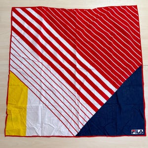 May include: A square bandana featuring a diagonal pattern of red and white stripes across the top and center. The bottom left corner has a solid yellow block, while the bottom right corner is a solid navy blue triangle with the FILA logo in white.