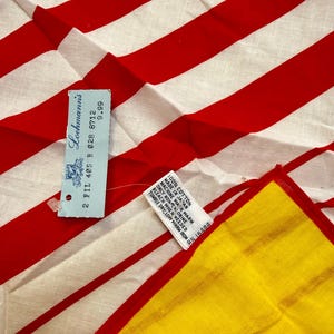 May include: A textile featuring bold red and white vertical stripes. A light blue rectangular tag is attached, displaying the text Loehmann's, 2 FIL 40S B 028 8712, and 9.99. A white care label reads 100% COTTON, MADE IN JAPAN, and care instructions.