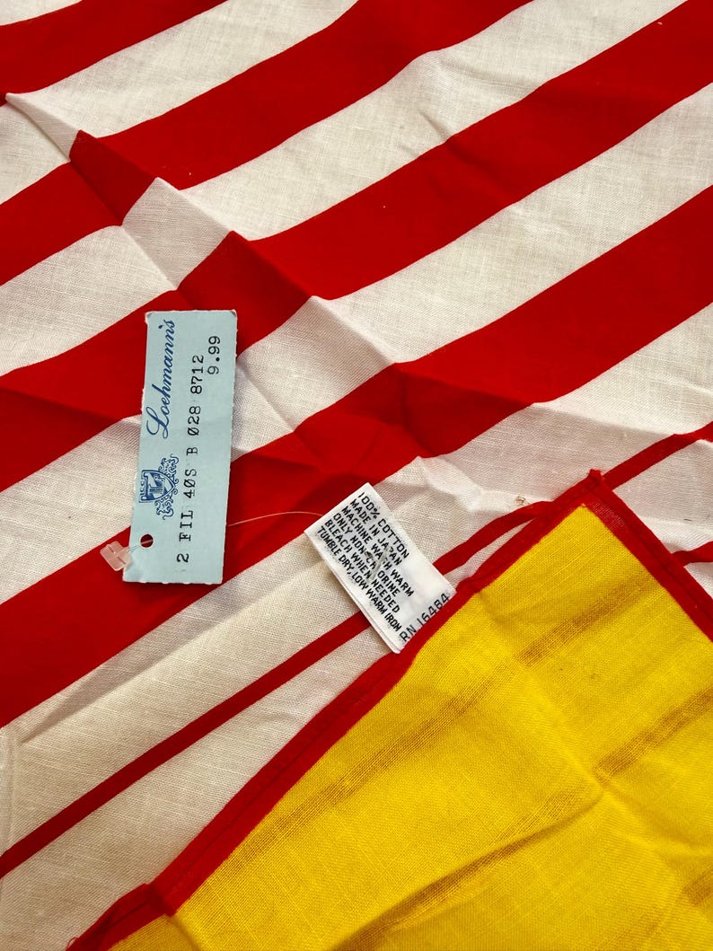 May include: A textile featuring bold red and white vertical stripes. A light blue rectangular tag is attached, displaying the text Loehmann's, 2 FIL 40S B 028 8712, and 9.99. A white care label reads 100% COTTON, MADE IN JAPAN, and care instructions.