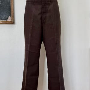 May include: Brown dress pants displayed on a mannequin. The pants have a classic, straight-leg design with a button and zipper closure. The fabric appears to be a medium-weight material, suitable for various occasions. The pants are displayed on a black stand.
