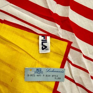 May include: A textile item featuring a pattern of bold red and white horizontal stripes. A white fabric tag with the black FILA logo is attached to the edge. A light blue rectangular paper tag is present with the text Loehmann's and 2 FIL 40S B 028 8712.