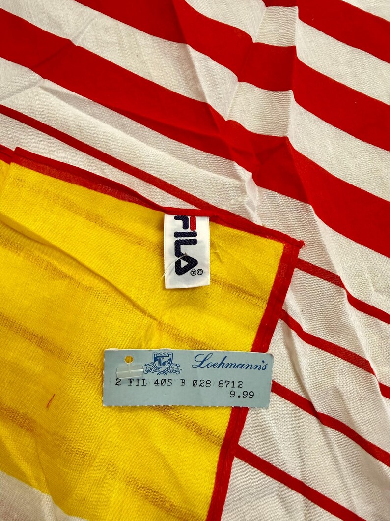 May include: A textile item featuring a pattern of bold red and white horizontal stripes. A white fabric tag with the black FILA logo is attached to the edge. A light blue rectangular paper tag is present with the text Loehmann's and 2 FIL 40S B 028 8712.