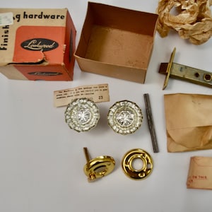 May include: An assortment of vintage door hardware, including two crystal-like doorknobs, a latch, and a strike plate. The hardware is accompanied by a cardboard box with the "Lookwood" logo, small paper packets, and a metal rod.