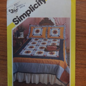 Peut inclure: Une enveloppe de patron de couture Simplicity présentant un modèle de couvre-lit et d'oreillers. L'image sur l'enveloppe montre un lit avec une courtepointe florale dans les tons de bleu, orange et jaune. L'enveloppe est jaune avec le logo Simplicity.