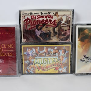 May include: Four music cassette tapes in clear plastic cases. The left tape is red with text reading Remembering Patsy Cline & Jim Reeves. The top center tape shows The Sons of the Pioneers. The bottom center tape is titled Country Memories. The right tape is titled Thanks for the Memories.