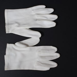 Könnte beinhalten: Ein Paar weiße Handschuhe, wahrscheinlich für formelle Anlässe, vor schwarzem Hintergrund. Die Handschuhe bestehen aus einem glatten Material und haben separate Fächer für Finger und Daumen.