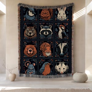 Könnte beinhalten: Eine gewebte Wohndecke mit einem Raster aus zwölf quadratischen Feldern, die jeweils eine andere Waldtierillustration zeigen, darunter ein Blauhäher, Eichhörnchen, Kaninchen, Waschbär, Specht, Biber, Stinktier, Maus, Rotkehlchen und Opossum auf schwarzem Hintergrund.