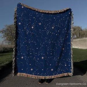 May include: A white ceramic mug with a black handle and the text "But First, Coffee" in a bold, black font. The mug is set against a blurred background, suggesting a cozy setting.