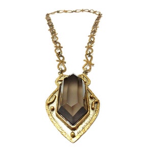 May include: A gold necklace with a large, faceted, smoky quartz pendant. The pendant is set in a gold frame with intricate details.
