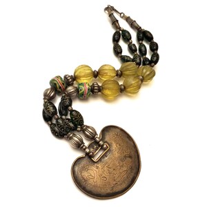 May include: A silver and brass necklace with green and yellow glass beads and a heart-shaped pendant with intricate engravings.